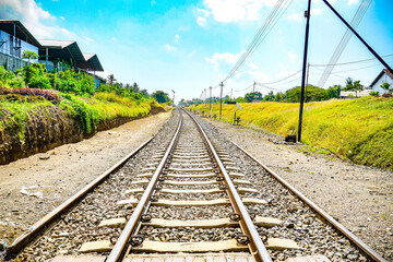 Old metal train track under  under bright blue sky and grass field