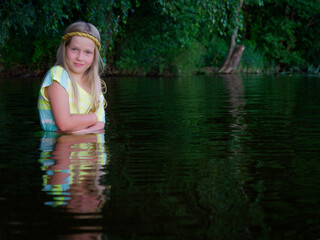 blonde girls with blue eyes bathes in clothes in the dark water of a lake at sunset