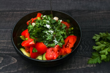Tomatoes and cucumbers vitamin salad in black bowl, wooden background. Healthy food concept.