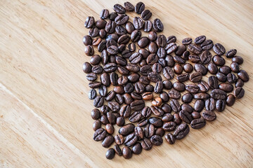 A heart-shaped made by roasted coffee beans on a light wooden background. Coffee lover concept background