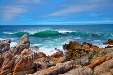 Fototapeta na wymiar Seascape of beautiful big waves with white foam hitting stone coastline on the sunny windy day, Cape Agulhas, Atlantic ocean, South Africa