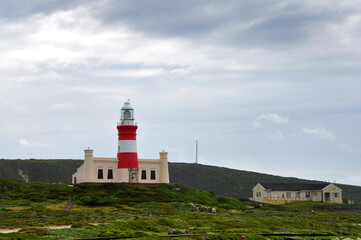Fototapeta na wymiar Landscape with the lighthouse on the beautiful rocky cliff on the windy day at Cape Agulhas, the most southern point of Africa, where the Indian and Atlantic oceans meet, South Africa