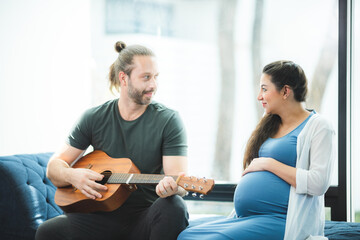 Husband plays guitar for pregnant wife at home