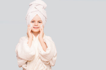 Smiling beautiful kid girl with towel on head hold cotton pad disk cleansing face skin with cleanser. Happy girl remove makeup enjoy healthy clean skincare beauty treatment concept