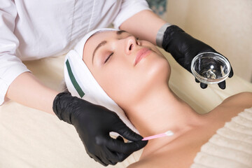 Cosmetologist doctor do enzyme theraphy procedure to a woman in her clinic. She wear glowes and mask