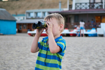 A boy with toy binoculars in his hands on the beach in summer.