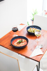 A served table with pasta and wine. Tomato pasta and pesto pasta with white and red wine on a wooden table in a restaurant