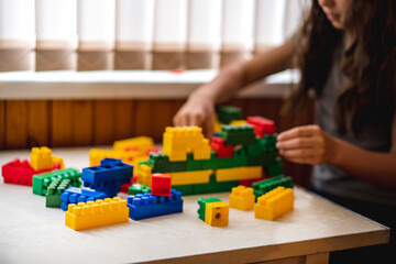 Happy little hirl child kid playing with colored plastic constructor on table in children room