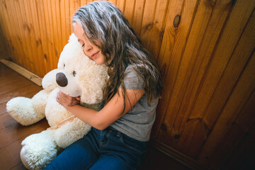 A beautiful little girl sits on the wooden floor and hugs Teddy bear a friend