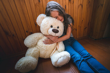 A beautiful little girl sits on the wooden floor and hugs Teddy bear a friend