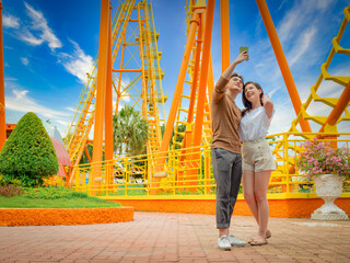 Young couple using a smartphone to take a photograph while visiting anamusement park. Young Couple Date Amusement Park Concept.