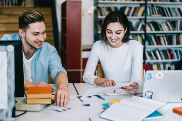 Smiling woman reading document and pointing with finger with student at table in library