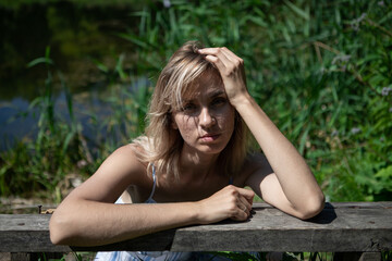 The girl with the blond hair on the lake shore rested her elbows and head on the bench. A thoughtful woman in a dress. Rest, relaxation, recuperation.