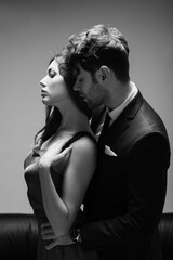 Fototapeta na wymiar Monochrome image of handsome man in suit kissing and embracing beautiful woman in dress on grey
