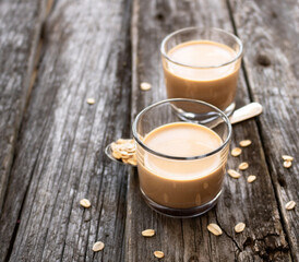 Vegan oat milk in glasses with a spoon and oat flakes scattered on an old wooden background.
