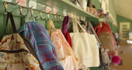 Backpacks hang on wall outside of classroom during school. 