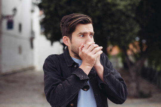 Young handsome man looks shocked, closes his mouth with his hands. A man outdoors looks scared and stressed