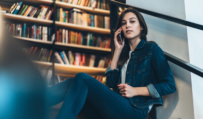 Satisfied young female student speaking on cellphone in library