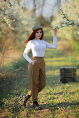  young beautiful red hair stylish  girl  seating on the boxes in apple  tree garden, pants and white turtleneck, natural background