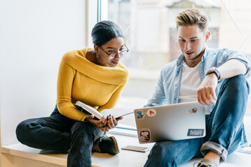 Pensive multicultural hipster students watching tutorial online on modern laptop device using...