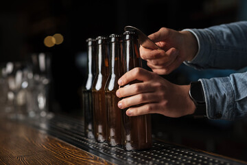 Beer festival. Bartender shirt opens bottles of beer on bar counter on blurred background