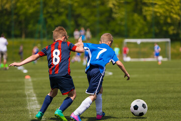 Two youth football players running in duel after ball. Kids kicking soccer match on the grass field. School children in sports jersey  clothes with numbers on back in tough competition