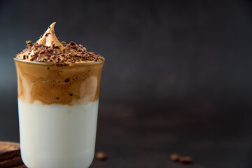 Close up of glass of trendy fluffy creamy dalgona or whipped instant coffee with milk and chocolate on the dark background. New popular food and drink trend concept. Copy space.