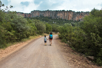 Fototapeta premium A woman with a backpack leads a child by the hand along a mountain trail.