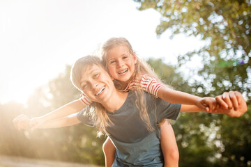 Happy children boy and girl frolic in the Park. The older brother plays with his sister in nature in the sunset rays of a summer day.