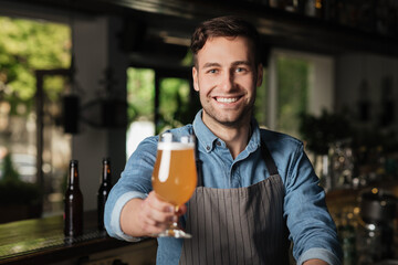 Light lager in glass. Bartender holds out hand with glass of light beer, for client