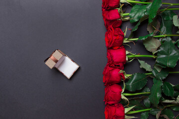Bouquet of red roses and opened brown gift box on black background, with copy space