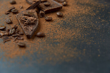 Dark chocolate stack, chips and cocoa powder with coffee beans on a dark background. Confectionery and food concept. Top view, copy space, selective focus..