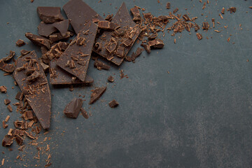 Dark chocolate stack, chips and cocoa powder on a dark background. Confectionery and food concept. Top view, copy space, selective focus..