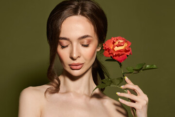 Beauty face of young woman with flower. Beauty treatment concept. Portrait of young woman with rose on green background.