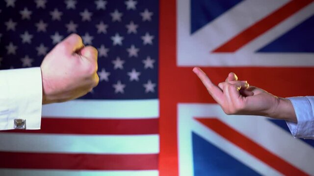 The United States and Great Britain threaten each other, showing signs with their fingers. Hand gestures on the background of flags. The conflict between the US and the UK