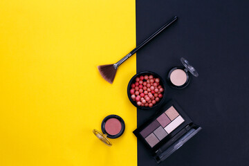 Blush in balls, eye shadow and cosmetic brush on a black and yellow background. View from above.