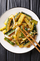 Japanese fried zucchini with onions and sesame seeds in soy sauce close-up in a plate on the table. Vertical top view from above