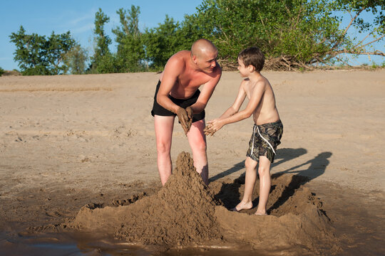 Dad and son build sand castles on the beach and laugh. Photo on the beach on a Sunny day. Family holiday