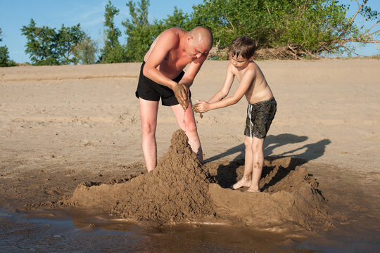 Dad and son are building sand castles against a background of green trees. Photos on the beach on a Sunny day