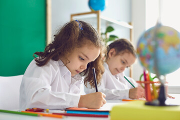 Back to school. Children schoolchildren write while sitting at the table in the classroom.