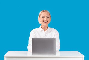 Cheerful mature business lady working with laptop at desk on blue background