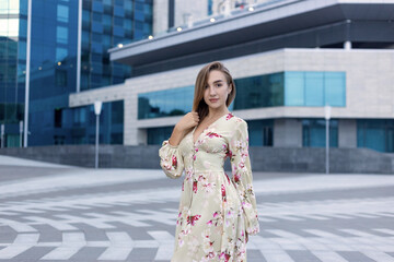 Portrait of a beautiful young girl on a background of a blue business center dressed in a summer beige dress