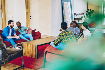 Crew of creative male and female colleagues sitting at loft interior coworking space communicating,...