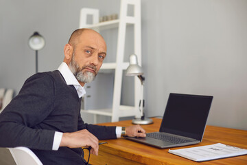 Online job concept. Serious elderly man working or studying at home on his laptop computer, mockup for design