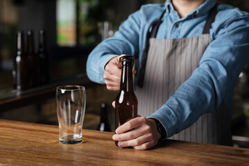 Trendy pub and brewery. Barman in apron opens bottle of beer