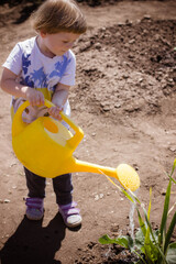 little boy watering a plant in a garden from a yellow watering can