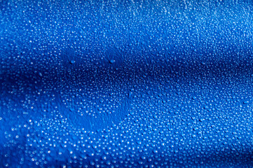 Abstract blue background with shadows with drops of water and a painted smiley with selective focus on a wet surface.
