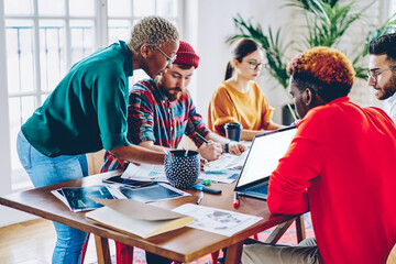 African american female leader checking work of crew helping with making planning accountings,  coach of crew training employees during workshop, colleagues cooperating and helping  each other.