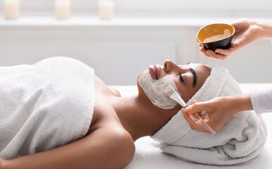 Beautician applying detox mask on black woman face