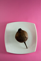 Red beet root vegetable lies in a white plate on a pink background.